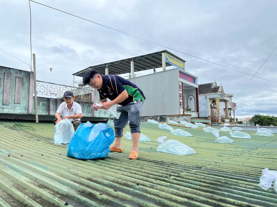 Anh Phan Thanh Sơn (áo trắng) cùng người thân trong gia đình đang chèn các bao nước trên mái nhà. Ảnh: Phương Dung z7194204478473-b3dbd057f6f592733cc6c0b2aa129811.jpg